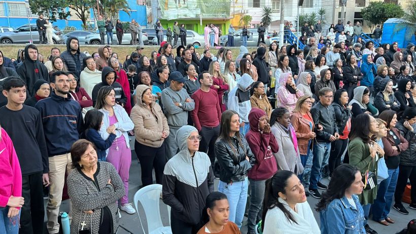 A large crowd of people standing together outdoors, some wearing hoodies or jackets, attentively observing an event in a public space.