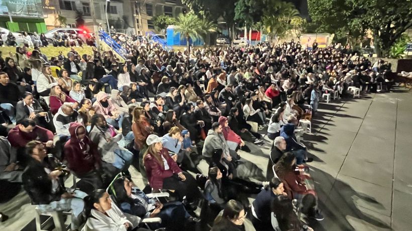 A large crowd of people sitting outdoors, gathered for an event or performance at night.