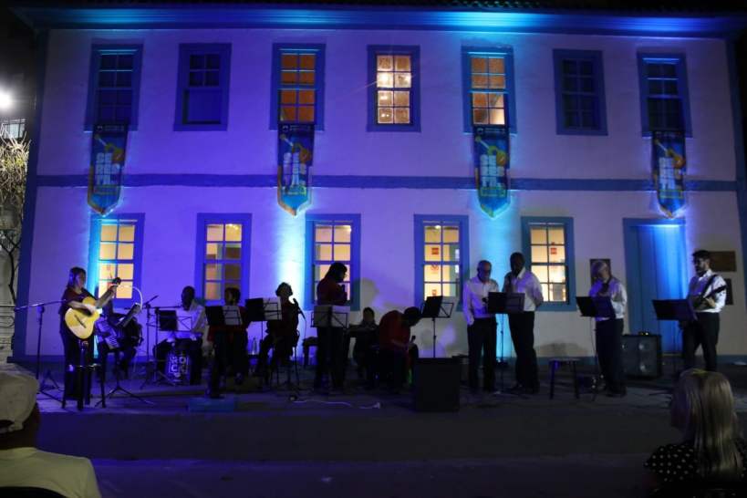Apresentação musical ao ar livre na Praça da Catedral, com músicos e cantores se apresentando sob luzes azuis, promovendo o evento Seresta na Praça.