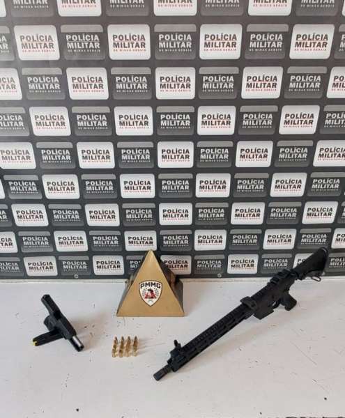 Imagem de armas apreendidas pela Polícia Militar, incluindo um fuzil Taurus T4 calibre 5.56, uma pistola calibre 9mm G3, cartuchos e um distintivo da PMMG em fundo com logotipo da Polícia Militar.