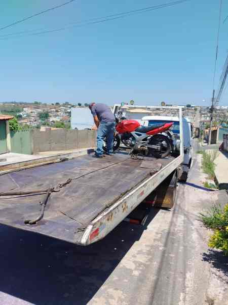Um homem carregando uma motocicleta vermelha Twister em um guincho em uma rua residencial, com casas ao fundo.