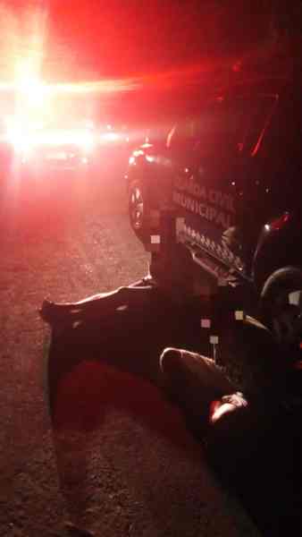 Imagem noturna com um veículo da Guarda Civil Municipal, iluminado por luzes de emergência, e uma pessoa no chão, possivelmente em uma situação de abordagem policial.