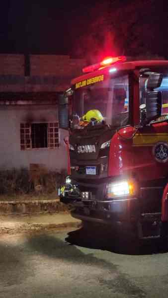 Caminhão dos bombeiros com luzes de emergência ativadas, estacionado em frente a uma residência durante a noite.