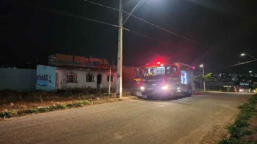 Caminhão do Corpo de Bombeiros estacionado em frente a uma residência aparentemente abandonada durante a noite, com luzes de emergência acionadas.