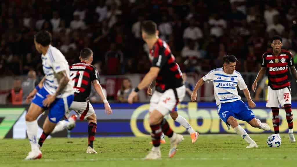 Jogadores de Cruzeiro e Flamengo em ação durante o jogo no Maracanã, com a bola em movimento e torcedores ao fundo.