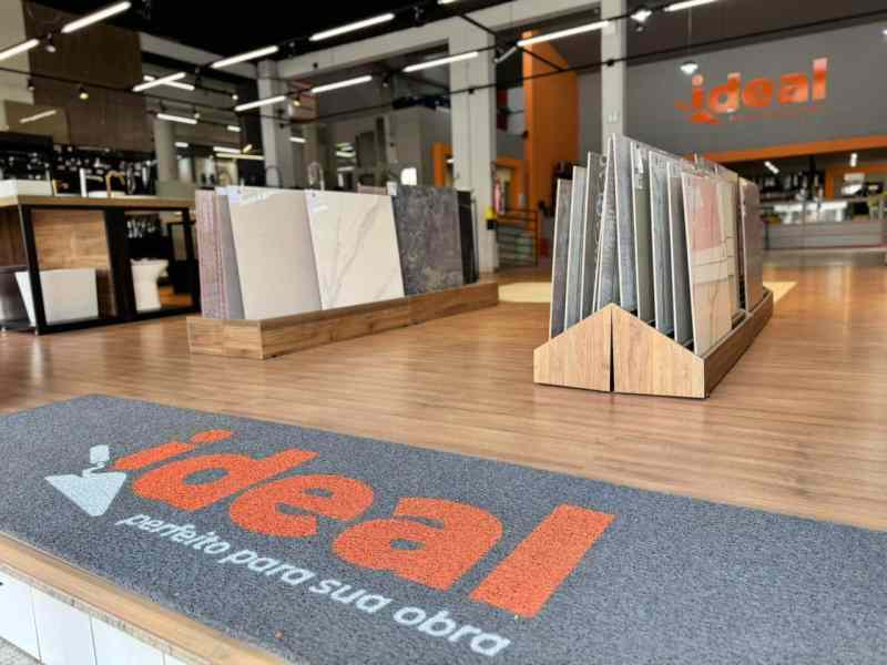 Interior da loja Ideal com exibição de peças de acabamento e piso, destacando o logotipo da marca no tapete de entrada.