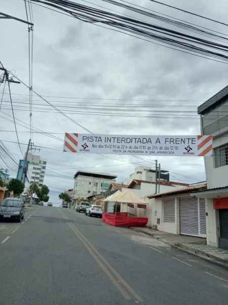 Faixa de interdição de pista na rua, informando sobre a restrição de acesso devido às celebrações em homenagem a Nossa Senhora da Conceição Aparecida.