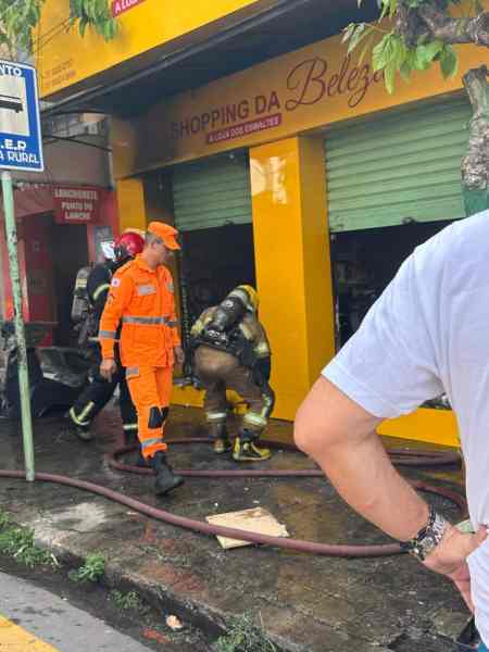 Bombeiros atuando no combate a um incêndio em uma loja de cosméticos, com destaque para as equipes e a fachada amarela da loja.