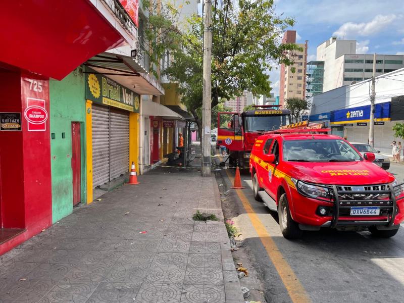 Cenas de um incêndio em uma loja de cosméticos na Avenida Primeiro de Junho, em Divinópolis, com um caminhão dos bombeiros e viatura na rua, enquanto a área está isolada com cones.