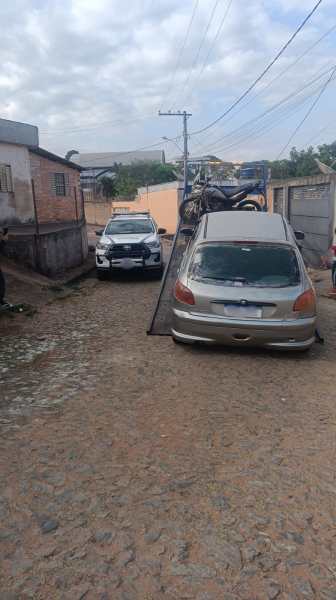 Um veículo sendo rebocado em uma rua de paralelepípedo, com um carro de polícia estacionado próximo.