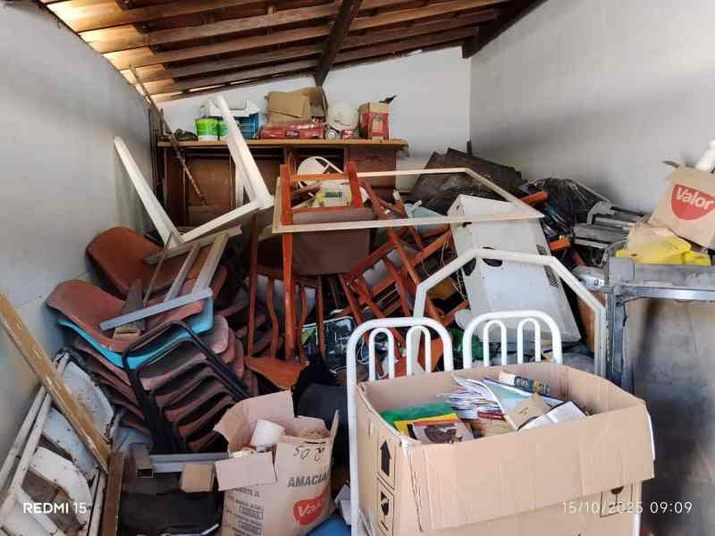 Uma sala desordenada cheia de cadeiras empilhadas, caixas de papelão e outros objetos acumulados.