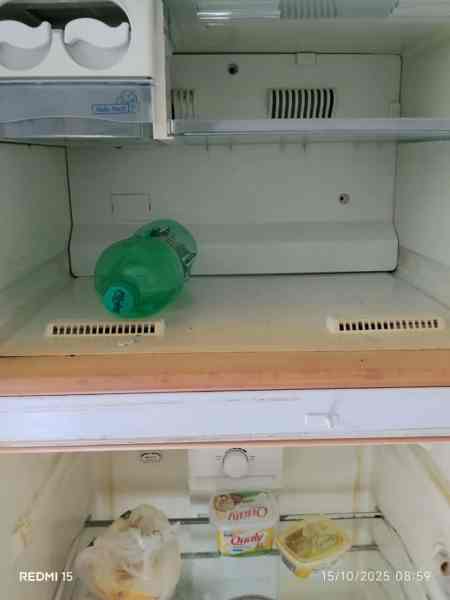 Interior de uma geladeira vazia com uma garrafa verde e alimentos armazenados de forma inadequada.