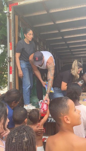 Grupo de pessoas doando brinquedos e doces de um caminhão para crianças em um evento social.