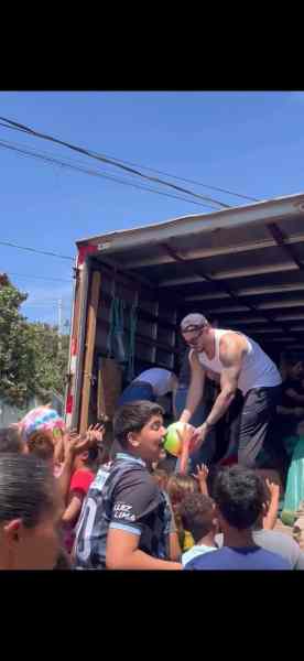 Thiago Verli hand-delivering toys to a crowd of excited children from a truck during a charitable event.