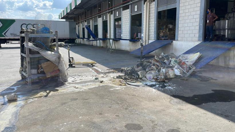 Área externa da empresa Cofer Atacadista em Carmo do Cajuru, com destroços de produtos inflamáveis queimados e empilhados no chão, após um incêndio.