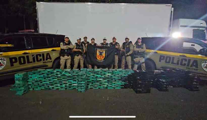 Foto da Polícia Militar Rodoviária de Minas Gerais posando em frente a um caminhão e uma grande apreensão de tabletes de cocaína dispostos em pilhas na estrada durante a Operação Rota Narco.