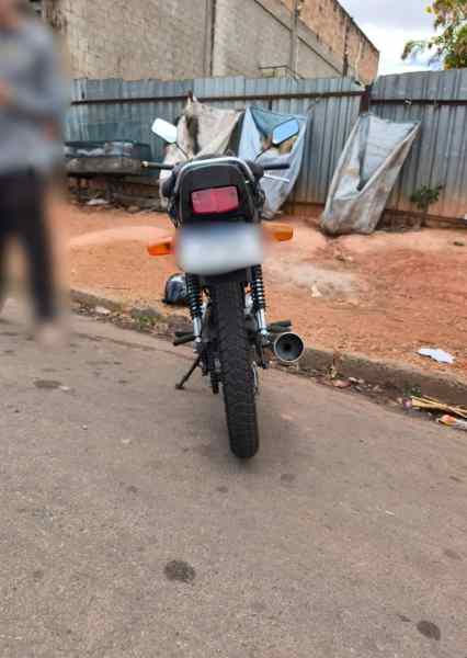 Motocicleta apreendida com escapamento irregular e sem placa visível, em ambiente urbano.