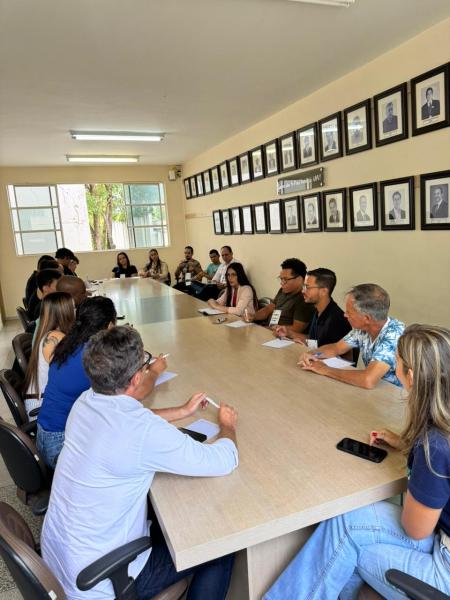Reunião de líderes de organizações sociais participando do Curso de Captação de Recursos, em um ambiente com uma mesa e diversas pessoas sentadas, com retratos emoldurados nas paredes ao fundo.