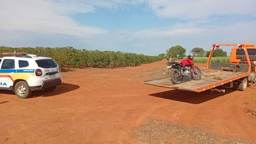 Viatura da Polícia Militar estacionada em um terreno agrícola, com uma motocicleta sendo transportada em um reboque.