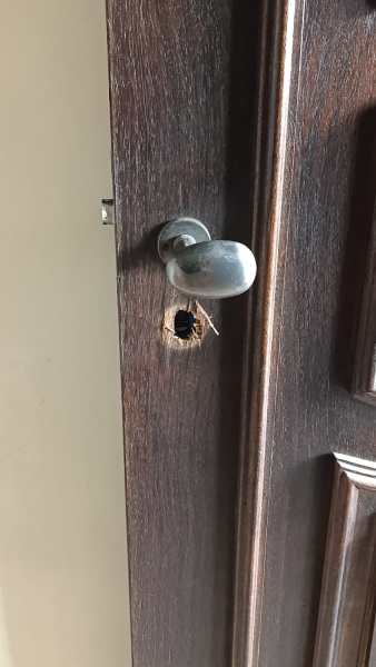 Fechadura danificada de uma porta, com buraco visível na madeira ao redor do local da maçaneta.