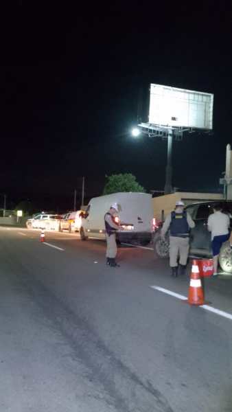 Policiais abordando um veículo durante uma operação noturna na rodovia, com cones de segurança visíveis e sinalização ao fundo.