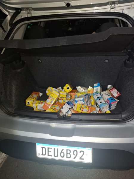 Tampa do porta-malas de um carro com várias caixas de leite e suco jogadas no fundo.