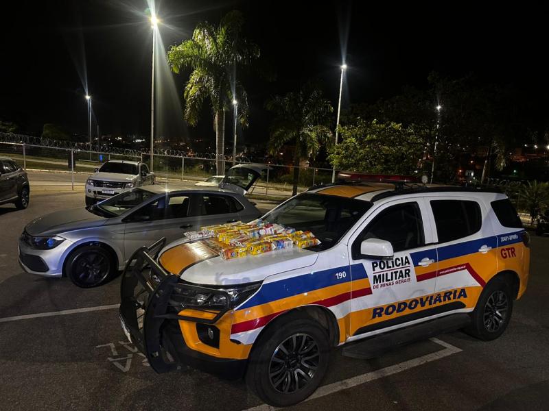 Veículo da Polícia Militar Rodoviária estacionado à noite, com produto em destaque no capô, rodeado por outros carros.