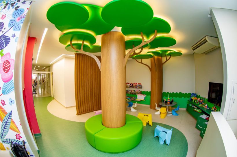 Espaço infantil colorido na ala de Oncopediatria, apresentando árvores decorativas, brinquedos e áreas de recreação para crianças em tratamento.