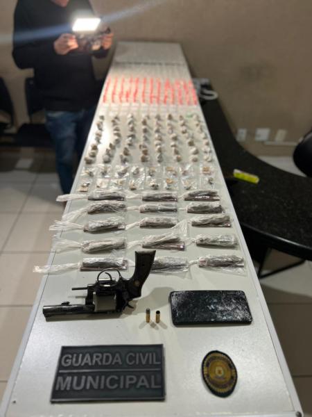 Mesa apresentando drogas, um revólver calibre .38, munições, e um celular, tudo apreendido pela Guarda Civil Municipal de Nova Serrana.