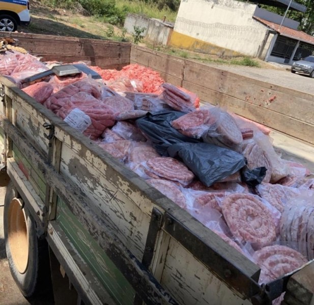 Caminhão de madeira carregado com pacotes de carne e linguiça, mostrando diversos produtos embutidos, alguns em condições inadequadas.