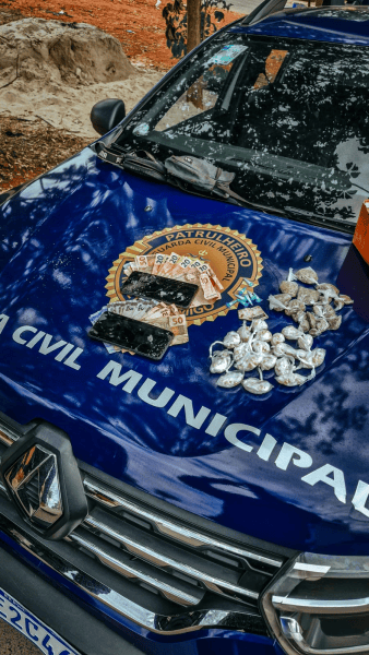 Veículo da Guarda Municipal com drogas apreendidas em cima do capô, incluindo pacotes de maconha, pedras de crack, e dinheiro.