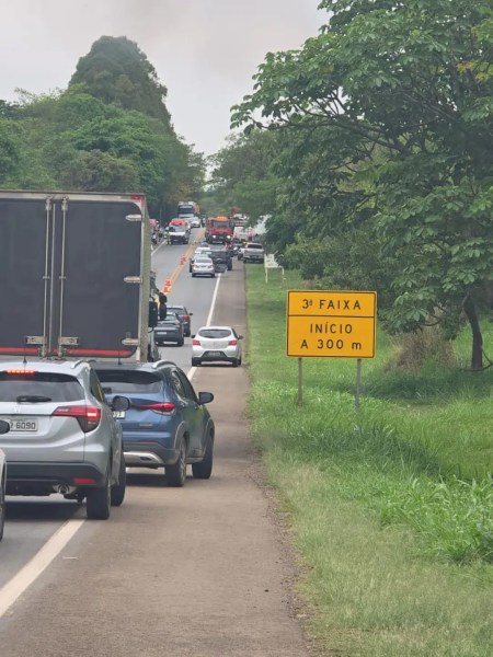 Imagem mostrando a rodovia MG-050 com tráfego intenso após um acidente, incluindo veículos parados e um sinal indicando o início de uma terceira faixa a 300 metros.