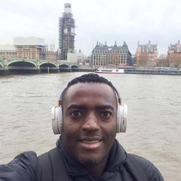 Selfie de um homem sorridente usando fones de ouvido, com o rio ao fundo e a famosa estrutura da Elizabeth Tower (Big Ben) em reforma.