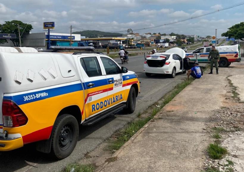 Veículo da Polícia Militar Rodoviária em ação de fiscalização de trânsito, com um Toyota Corolla branco parado ao lado e autoridades inspecionando.