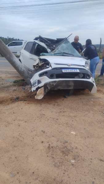 Veículo FIAT/Punto severamente danificado após colisão com poste de energia elétrica em rodovia, com presença de pessoas avaliando a situação.
