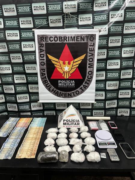 Material apreendido pela Polícia Militar, incluindo drogas, dinheiro e equipamentos relacionados ao tráfico, em uma mesa com logo da PM ao fundo.