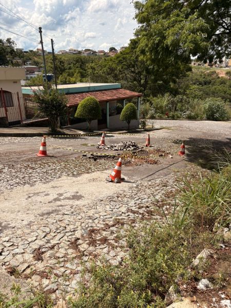 Buraco na Rua José de Alencar, cercado por cones e fitas, indicando uma obra inacabada da Copasa e causando transtornos aos moradores.
