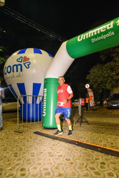 Corredor atravessando arco de chegada em evento noturno, com balão promocional ao fundo.