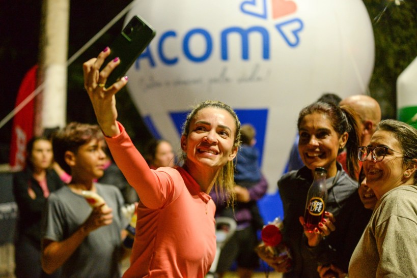 Grupo de pessoas sorrindo e tirando uma selfie em um evento, com uma bola inflável ao fundo mostrando a marca da Acom.
