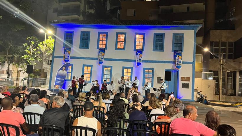 Público assistindo ao evento Seresta na Praça, com apresentação musical em frente a uma casa histórica iluminada.