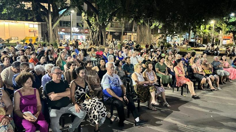Público sentado na Praça da Catedral durante o evento Seresta na Praça, com uma grande variedade de pessoas assistindo ao espetáculo à noite.