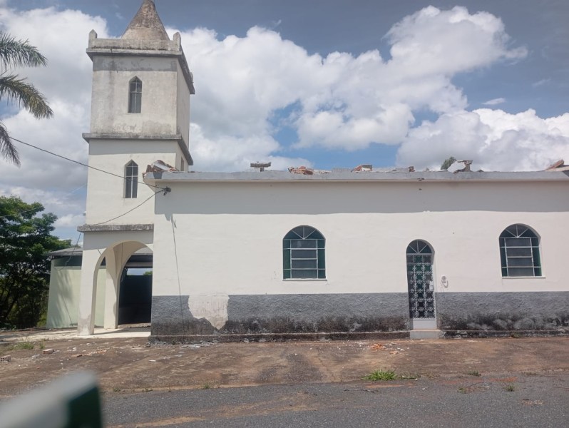 Igreja com danos visíveis no telhado após vendaval, mostrando estrutura metálica exposta e pedras ao redor.
