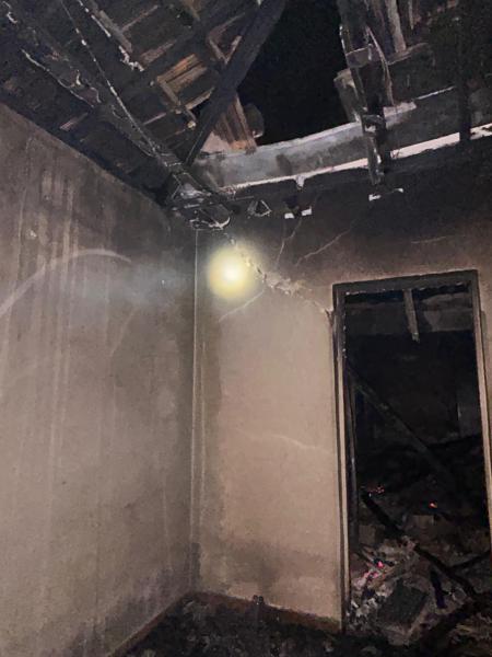Interior de um imóvel abandonado com danos significativos causados por um incêndio, incluindo paredes carbonizadas e um teto desmoronado.