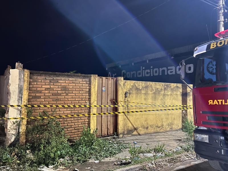 Portão de um imóvel abandonado, cercado com fita de segurança dos bombeiros, durante a noite.
