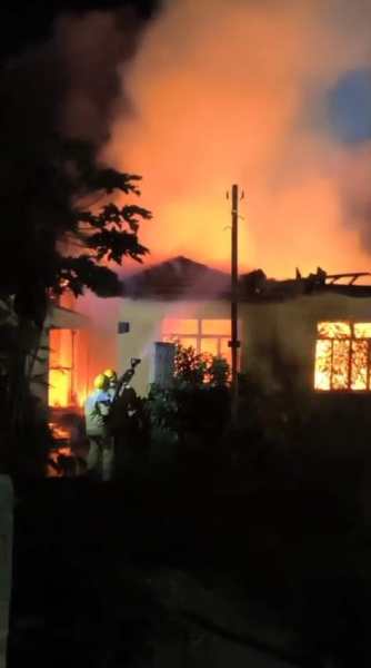 Incêndio em imóvel abandonado com chamas visíveis nas janelas e fumaça no ar, durante a atuação do Corpo de Bombeiros.