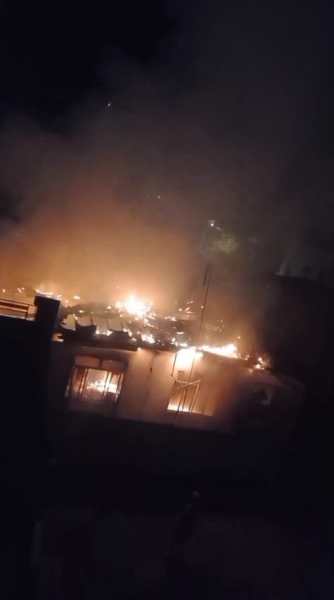 Incêndio em imóvel abandonado com chamas e fumaça visíveis, iluminando a cena à noite.