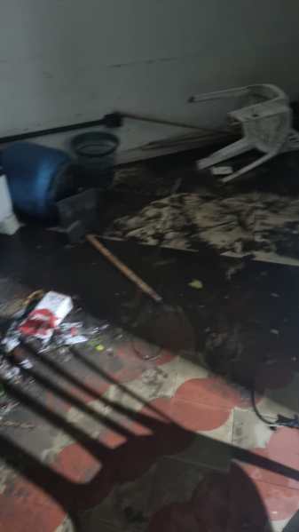Interior de uma casa mostrando danos causados por alagamento, com móveis deslocados e sujeira no chão.