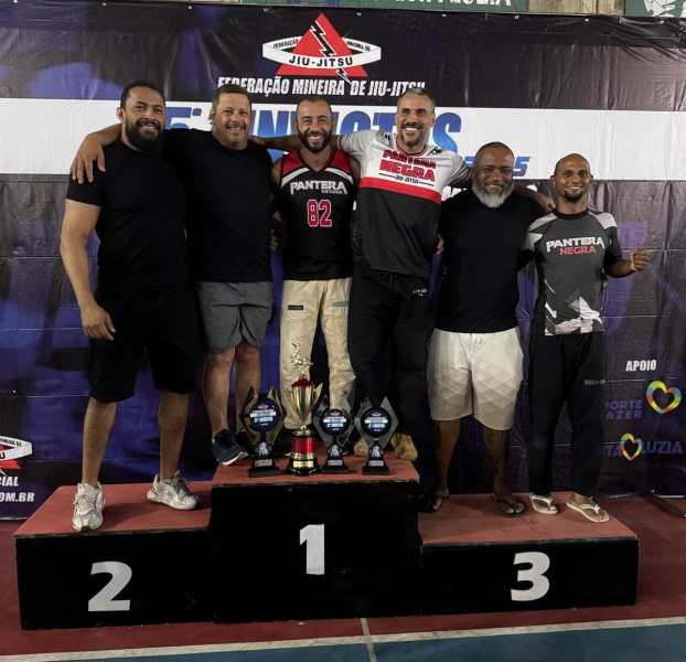 Grupo de professores da equipe Pantera Negra de Jiu-Jitsu celebrando a conquista no pódio do campeonato, exibindo troféus e medalhas.