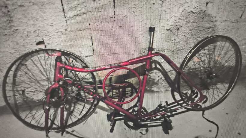Bicicleta desmontada de cor vermelha, com as rodas e outros componentes visíveis, colocada contra uma parede de tijolos.