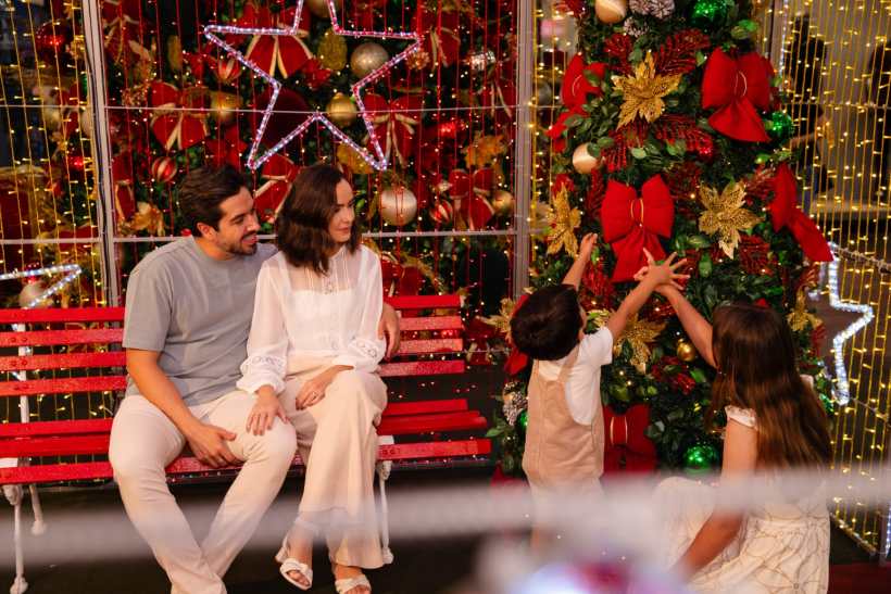 Família reunida em um ambiente decorado para o Natal, com uma árvore de Natal ornamentada e luzes festivas, em um espaço acolhedor de shopping.